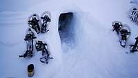 Links und rechts vor dem Ausgang einer Schneehöhle liegen die Schneeschuhe der Soldaten.
