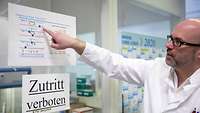Ein Mann im Laborkittel zeigt auf ein Plakat