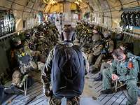 Ein Soldat von hinten gesehen steht im Laderaum eines Flugzeuges vor sitzenden Soldaten