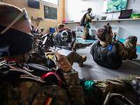Mehrere Soldaten sitzen am Boden in einem Raum, vor ihnen steht ein Soldat am Laptop und Monitor