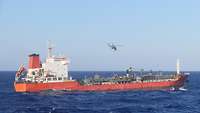 Ein oranges Schiff fährt auf dem Wasser und ein Hubschrauber fliegt über dem Schiff