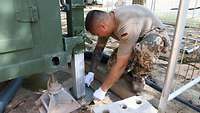 Ein Soldat kniet neben einem Container und baut den Fuß einer Stütze für eine Kontrolle und Reinigung aus