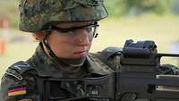 Eine Rekrutin beobachtet mit einem Gewehr G36 im Anschlag das vor ihr liegende Gelände.