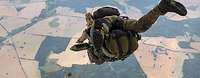 Ein Soldat mit Ausrüstung und Gepäck springt aus einem Flugzeug