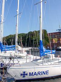 Im Bootshafen der Marineschule Mürwik liegen mehrere Segelboote. Im Hintergrund ist die Marineschule zu sehen. 