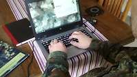 Ein deutscher Soldat sitzt in Uniform zu Hause an einem Rechner im Homeoffice.