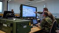 Zwei Soldaten sitzen vor einem großen Monitor.