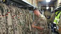 Ein Soldat steht in einem Lager mit Dienstbekleidung und überprüft den Bestand