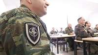 Ein griechischer Ausbilder trägt das Abzeichen der NATO-School auf dem Ärmel.