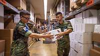 Zwei Soldaten in einem Lager hantieren mit Paketen