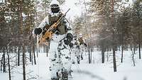 Mehrere Soldaten im Schneetarn laufen auf Skiern hintereinander durch einen verschneiten Wald.