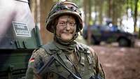 Eine Soldatin mit Tarnschminke im Gesicht und Helm steht vor einem Fahrzeug.