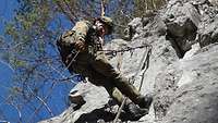 Ein Soldat in Gebirgsjägeruniform klettert an einem Seil eine Felswand hinauf.