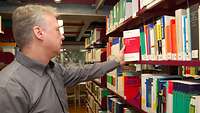 Ein Mann nimmt in der Bibliothek ein Buch aus dem Regal.
