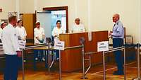 Personal der Truppenküche Führungsakademie Hamburg Männliche Person in Uniform spricht zu mehreren Personen in Küchenkleidung in einem Speisesaal