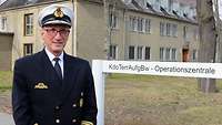 Ein Admiral steht vor einem Wegweiser zur Operationszentrale. Im Hintergrund ein Gebäude.