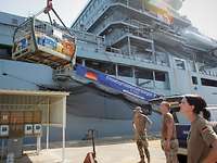 Proviantübernahme Interview Marinesanität Ein graues Marineschiff im Hafen hebt eine Gitterpalette mit einem Bordkran an Bord.