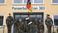 Soldaten, darunter einer mit Truppenfahne, vor einem Gebäude mit dem Schriftzug Panzerbataillon 363.