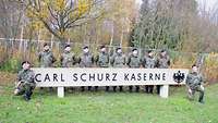 Soldaten stehen hinter einem Schild der Schrift „Carl Schurz Kaserne“ neben der Kaserneneinfahrt.