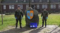 Zwei Soldaten des Objektschutzregiments stehen vor dem Verbandswappen. Sie unterstützen Bürgerinnen und Bürger