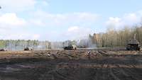 Vier Panzerhaubitzen 2000 stehen in ihrer Feuerstellung und verschießen Geschosse. Rauch steigt auf.