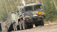 Ein Lkw lässt eine Wechselladepritsche ab. Ein Soldat überwacht den Vorgang an der Seite.