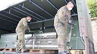 Zwei Soldaten stehen auf der Ladefläche eines LKW und entladen den LKW