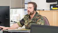 Soldat im Callcenter für Reservisten Ein Soldat mit kurzem Vollbart, in Tarnfleck-Uniform. Er hat ein Headset auf und telefoniert.