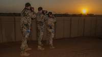 Zwei Soldaten und eine Soldatin stehen an der Campmauer und fotografieren die Abendsonne