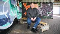 Ein Soldat in Zivil vor einer Grafitti-Wand.