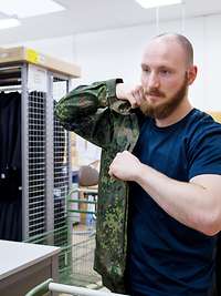 Ein Mann im zivilen T-Shirt zieht sich eine Feldjacke der Bundeswehr an, um deren Größe zu prüfen