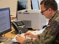 Ein Soldat im Vordergrund an einem PC-Arbeitsplatz, einer im Hintergrund