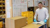 Beamter der Poststelle steht vor den Regalen mit Postboxen und notiert im Postbuch empfange Pakete.