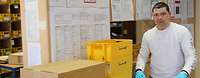 Beamter der Poststelle steht vor den Regalen mit Postboxen und notiert im Postbuch empfange Pakete.