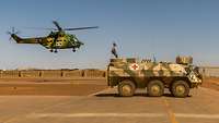 Ein rumänischer Hubschrauber schwebt in der Luft, rechts davor steht der Transportpanzer Fuchs der Sanitäter