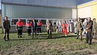 Viele Personen in Uniform, Schutzkleidung der Hilfsorganisationen und Schutzanzügen stehen vor einer Halle