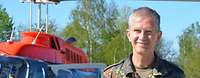 Ein Soldat im Feldanzug steht im Freien vor einem Hubschrauber und lächelt.