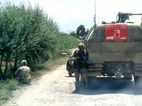 Deckung suchen hinter einem Fahrzeug Ein Soldat läuft auf unbefestigter Straße mit einer Waffe zur Rückseite eines Militärfahrzeuges.