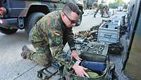 Ein Soldat kniet vor seinem Gepäck und verpackt sorgfältig seine Ausrüstung.