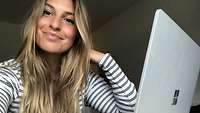 Selfie einer junge Frau mit blonden langen Haaren im Ringelshirt vor ihrem Laptop.