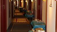 In einem Hotelflur steht neben jeder Tür ein Tisch. Auf diesem stehen Essenstabletts.