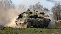 Ein Kampfpanzer in voller Fahrt von vorn, er wirbelt Staub auf.