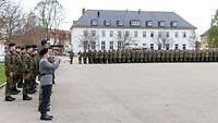 Soldaten sind auf einem Appellplatz in Formationen angetreten. Ein Soldat spielt auf einer Trompete.