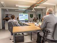 Infos zum JFAC Headquarter General Eberhard Zorn sitzt mit Soldaten in einem Konferenzraum bei einem Powerpoint-Vortrag.