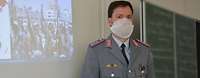 Soldat im Dienstanzug steht vor einer grünen Tafel. Wegen der Corona-Krise trägt er eine Gesichtsmaske aus Papier.