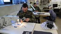 Zwei Soldaten sitzen hintereinander an einer Nähmaschine und nähen Schutzmasken.