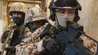 Drei Soldaten stehen mit ihren Waffen im Anschlag hintereinander vor einer Tür.