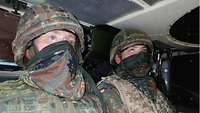 Zwei Soldaten mit Dreieckstuch über Mund und Nase sitzen im Gefechtsfahrzeug