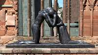 Skulptur Versöhnung mit zwei umarmenden Menschen vor einer Kirche