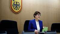 Annegret Kramp-Karrenbauer sitzt vor einem Wappen mit Bundesadler 